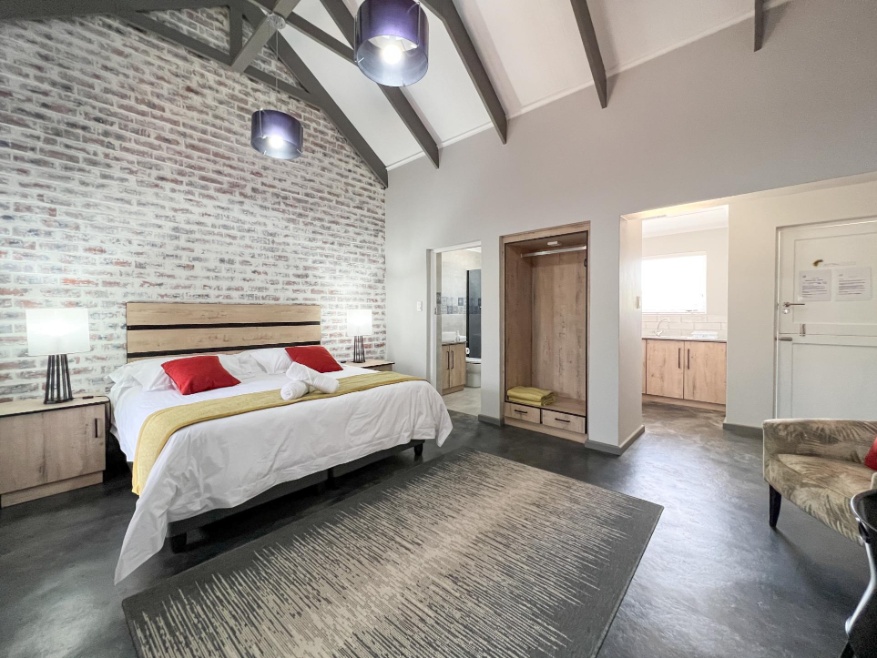 Air-conditioned luxury self-catering unit with high-speed free Wi-Fi, king-size bed, bedroom cupboard wardrobe layout, and an adjacent fully equipped kitchen view at a secure Oudtshoorn guest estate.