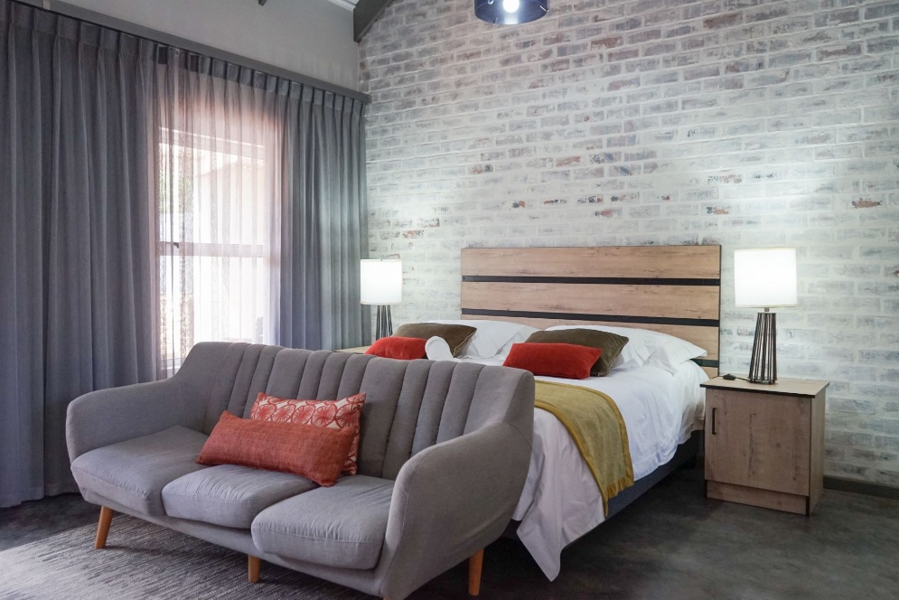 Air-conditioned executive bedroom with a flat-screen TV setup, king-size bed, private lounge sofa, and high-speed free Wi-Fi access at an Oudtshoorn guest estate.