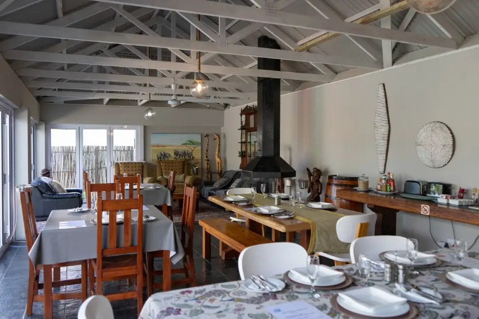 Large communal dining hall and breakfast room layout with set tables and a central fireplace at a group guest lodge in Oudtshoorn.