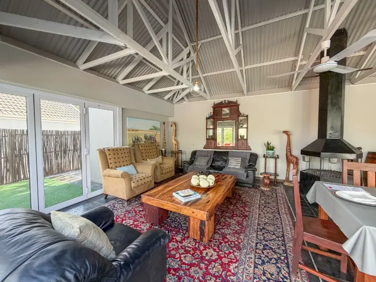Communal lapa braai area and indoor entertainment lounge with rustic wooden table and fireplace at a group accommodation estate in Oudtshoorn.